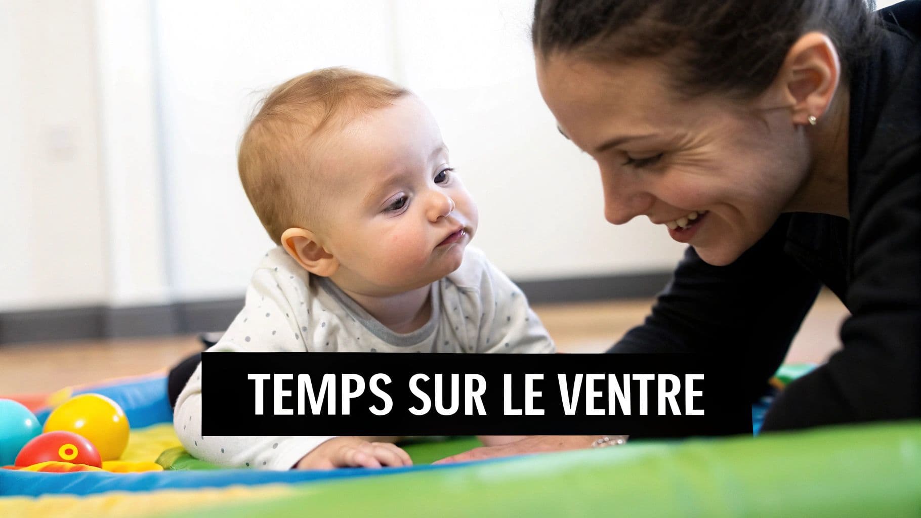 Bébé souriant fait du temps sur le ventre sur un tapis d'éveil, regardant une femme joyeuse.