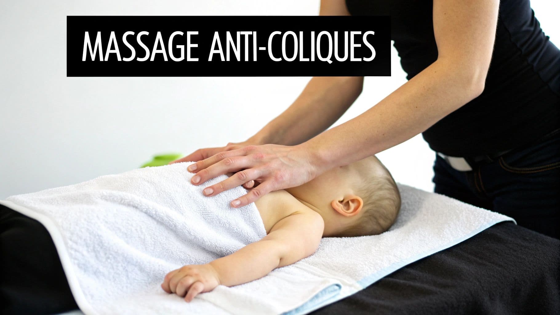 Une personne masse doucement le ventre d'un bébé allongé sur une serviette, pour soulager les coliques.