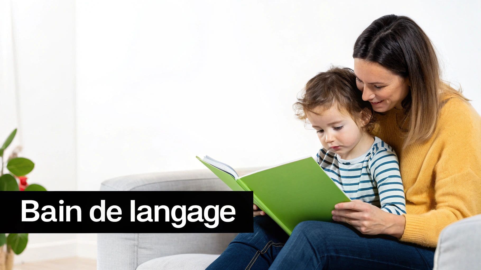 Bain de langage : une mère et son jeune enfant lisent ensemble un livre vert sur un canapé.
